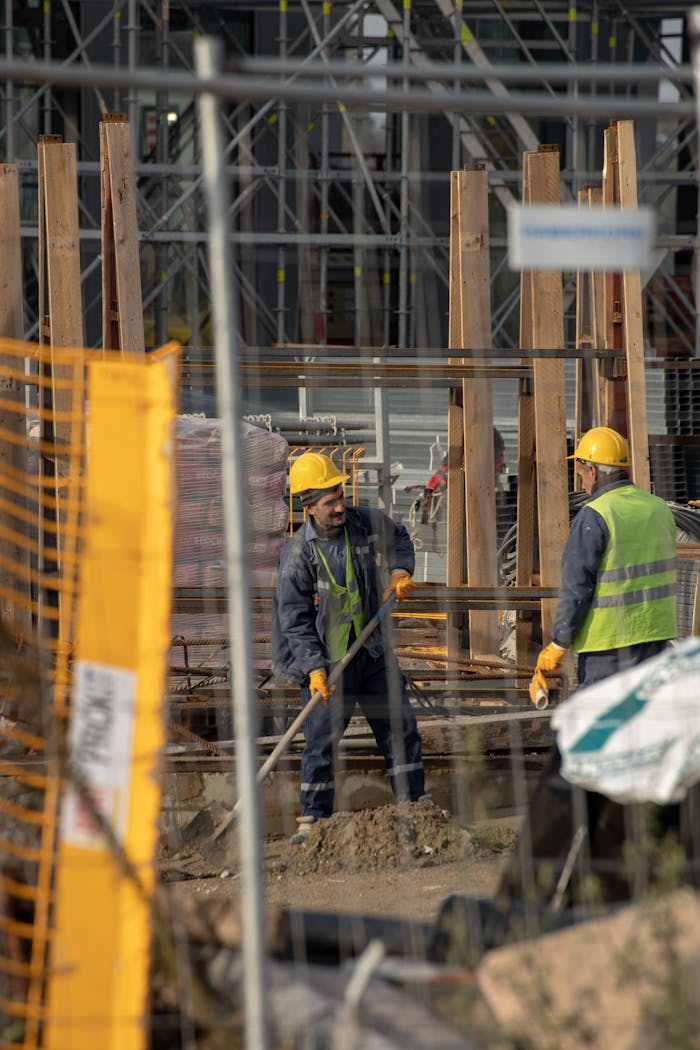 gallery-1 Construction workers in hard hats at an active building site with safety barriers.