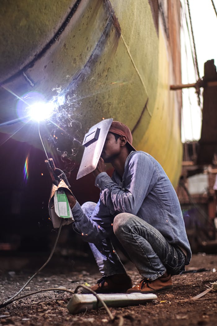 gallery-6 A worker wearing protective gear welds a ship hull at an outdoor shipyard.