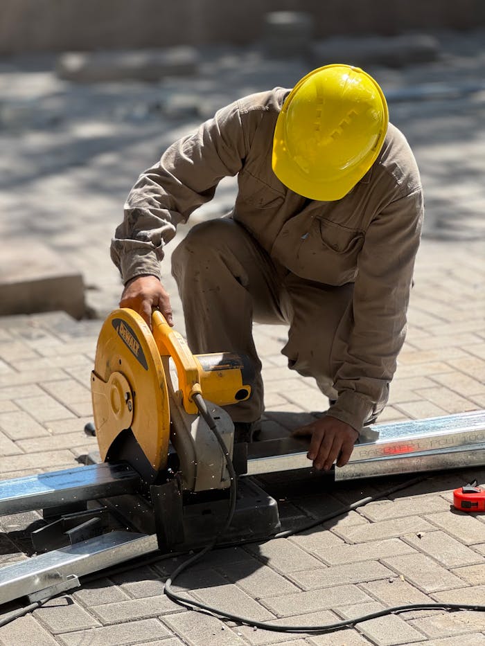 why-choose-us A construction worker wearing a yellow helmet cuts metal using a circular saw outdoors.