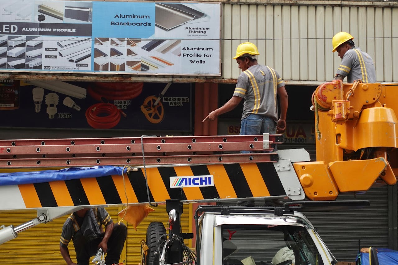 Two construction workers on a boom lift inspecting a building facade wearing safety helmets.