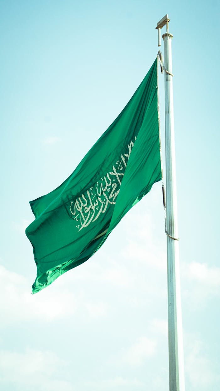 contact-img Vibrant Saudi Arabian flag waving high against a clear blue sky symbolizing national pride.