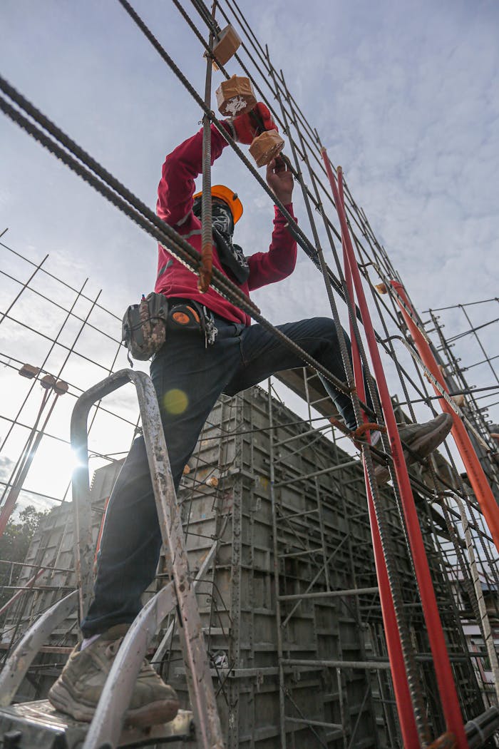 services-01 A construction worker wearing safety gear climbs a steel frame at an outdoor construction site.